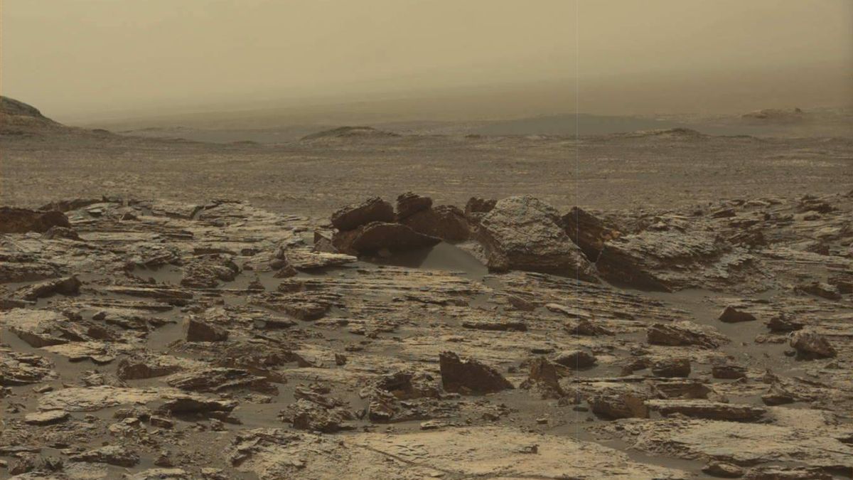 A dull yellow-tinted, rocky terrain blown with dust, as the sky in the distance matches the ground